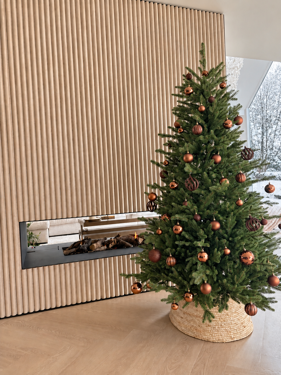 Kunstig juletre med kobberfargede julekuler ved peis