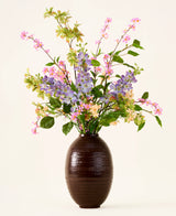 In een donkerbruine vaas staat een boeket van roze, paarse en gele Zijden kunstbloemen, het ‘Sky Kiss’-boeket, met groene bladeren, tegen een effen lichte achtergrond. Deze onderhoudsvrije decoratie zorgt voor blijvende schoonheid in elke ruimte, zonder dat er onderhoud nodig is.