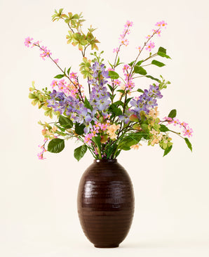 In een donkerbruine vaas staat een boeket van roze, paarse en gele Zijden kunstbloemen, het ‘Sky Kiss’-boeket, met groene bladeren, tegen een effen lichte achtergrond. Deze onderhoudsvrije decoratie zorgt voor blijvende schoonheid in elke ruimte, zonder dat er onderhoud nodig is.