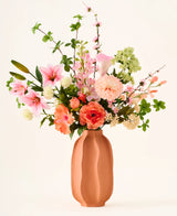 In een terracotta vaas staat het kleurrijke boeket ‘Yasmine’s Choice’ van zijden kunstbloemen, bestaande uit roze lelies, perzikkleurige rozen en groen blad, vervaardigd uit hoogwaardige zijden bloemen van Easyplants, allemaal prachtig gearrangeerd tegen een lichte achtergrond.