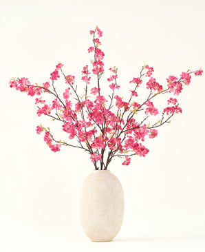 De Zijden kunstbloemen boeket Kersenbloesem fuchsia 150 cm heeft levendige fuchsia kersenbloesem stelen met groene bladeren in een eenvoudige witte vaas, die een aanvulling is op elk interieur tegen een lichte achtergrond.